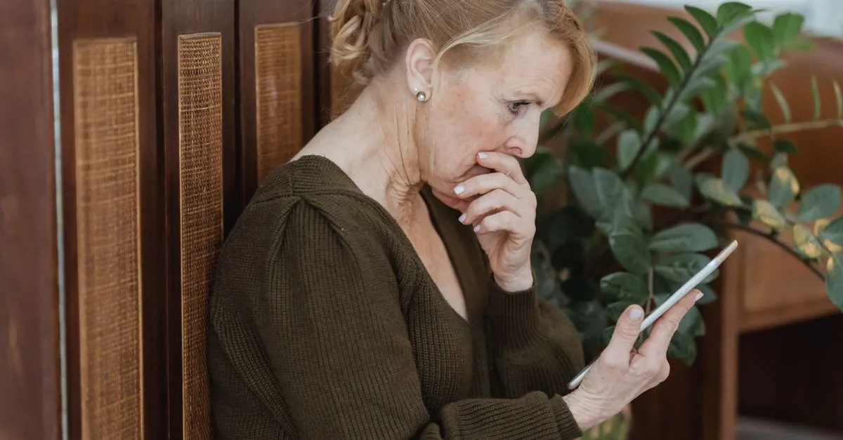 A woman reading a message on her phone with a concerned expression.