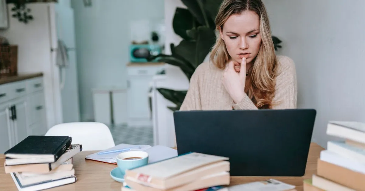 Woman studying online on a laptop at a table stacked with books and coffee, researching an answer the way Perplexity reads a page.