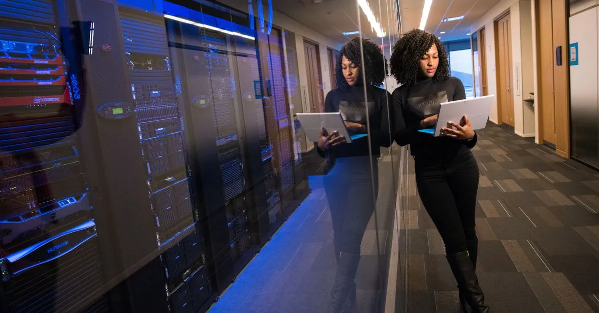 A woman reviewing a tablet beside a row of mirrored servers in a modern data center.