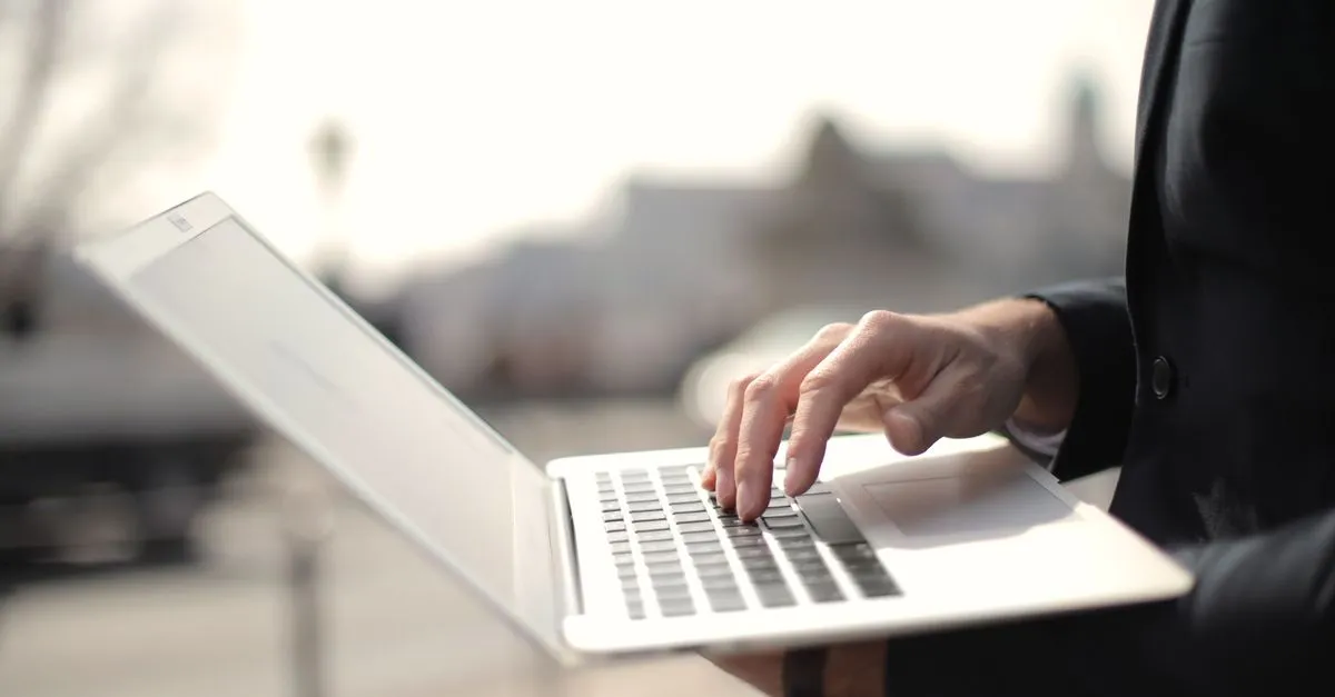 A business professional typing on a laptop, filling out an online form.